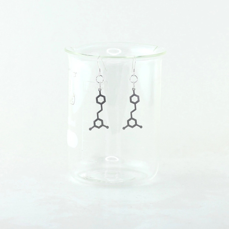 A pair of stainless steel earrings of resveratrol molecules displayed on a glass bottle