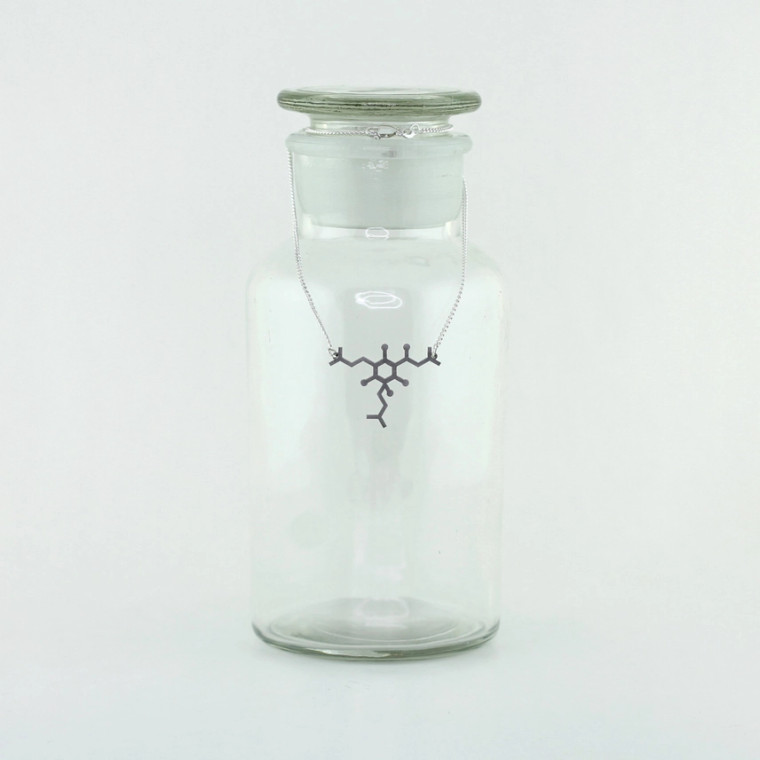 A stainless steel necklace of a humulone molecule displayed on a glass bottle