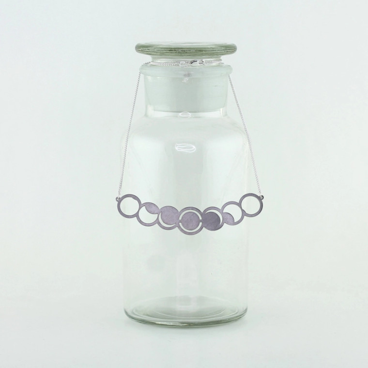 A stainless steel necklace of the solar eclipse sequence displayed on a glass bottle