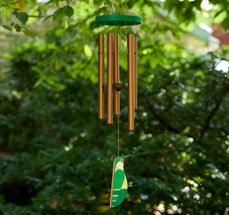 Picture of windchime hanging. Warm cord connects bronze colored tubes to a central hook, while a painted hummingbird acts as the wind sail. The wooden top of the windchime is green like the hummingbird.