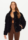 THE UPSIDE women's jet-black Amari Puffer Jacket made in plush velvet fabrication features full lining with an internal zip pocket, elasticated cuffs, adjustable cord at hem, front welt pockets, zip front with snap button closure, and an embossed horseshoe logo apple leather patch.