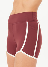 THE UPSIDE women's red recycled peached Samara 3.5inch Spin Short offers a soft & supportive fit and features side pockets and contrast cream stripes. Made for pilates.