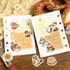 Calico Cat Welcome Meow stickers decorating open ring-bound planner pages beside a pretzel