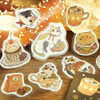 Calico Cat Welcome Meow stickers scattered loose on a wooden table beside a pretzel