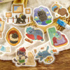 Cat's Atelier stickers of framed cat portraits and cat artists arranged on a woven fabric surface