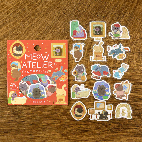 Cat's Atelier package with individual die-cut cat and artist studio stickers on a wood grain background
