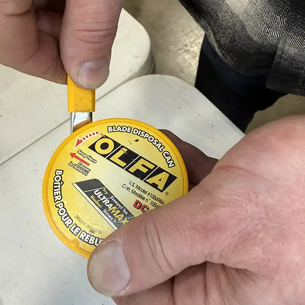 Professional installer changing OLFA snap blade on yellow utility knife during window film installation