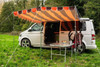 An image of the OLPRO Orange and Brown Campervan Canopy on the VW T5 Campervan in a field with a treeline in the background.