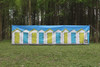 Beach Huts Design 4 Pole Compact Windbreak Steel Poles by OLPRO pictured on a field. It's Blue sky with White Beach huts with alternate blue and yellow doors fully assembled in a straight line.