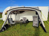 An image of the View Lite 390 Caravan Awning from OLPRO attached to a caravan in a field with some camping furniture inside of it.