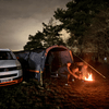 A family sits outside the Cocoon Breeze® v2 Campervan Awning wrapped in blankos surrounding a fire. 