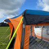 The Uno Breeze v2 Campervan Awning by Olpro photographed from from the front right corner, showing a brightly coloured storm strap, open main door & peak canopy ,imageset:Orange