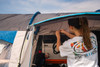 A camper rolling up the door & fly mesh on the side door of the Cocoon V2 Poled Campervan Awning by OLPRO