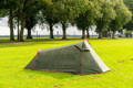 The OLPRO Beckford Lightweight 2 Person Tent pitched in a field with a treeline behind it with its doors closed, depicting a wild camping scene.