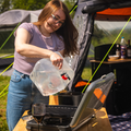 Image of a lady using the Folding 10L Water Carrier by OLPRO to fill a camping pan on a camping stove.
