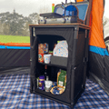 The OLPRO Bamboo Cooking Table can accommodate a cooking stove on top, with plates, cutlery, and food stored inside, accessible through the open zip doors within a campervan awning.