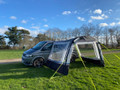 The Pershore Breeze® Campervan Canopy by OLPRO is attached to a grey Volkswagen T5 with the side doors closed.