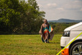 a young lady walking towards a camper van wearing the Vivid Spruce Insulated Outdoor Blanko Blanket as a poncho. imageset:Vivid Spruce