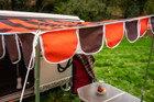 A close up of the material and poles of the OLPRO Orange and Brown Campervan Canopy that is attached to a Volkswagen Camper Van.