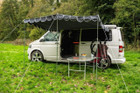 An image of the OLPRO Charcoal Campervan Canopy on the VW T5 Campervan in a field with a treeline in the background.