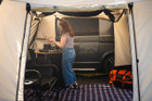 A young woman cooks on a CampinGaz stove atop a sustainable OLPRO Bamboo Camp Kitchen  Cubo Campervan Awning OLPRO