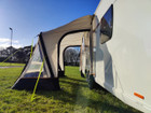 The OLPRO View Lite Breeze 260 Caravan Awning pictured attached to a caravan in a field with all of its doors open from a side angle.