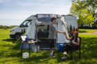 A couple shares a drink outside of the Loopo Breeze® XL v2 Motorhome Awning, they are using OLPRO camping furniture