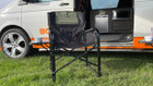 The OLPRO Directors Camping Chair in green and black with the side table up and a melamine mug in the cup holder pictured in front of a VW campervan with its sliding door open.