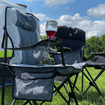 An image of a glass of wine being stowed in the wine glass holder of the Henwick Padded Folding Camp Chair - Grey & Charcoal from OLPRO outside of a tent.