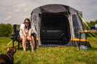 A woman sits in a camping chair outside the Loopo Breeze® v2 Campervan Awning, she is playing with a dog imageset:Charcoal