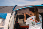 A camper rolling up the door & fly mesh on the side door of the Cocoon V2 Poled Campervan Awning by OLPRO