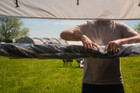 A man rolls up the canvas to reveal one of the large windows on the side panel of an OLPRO Pershore Breeze® Campervan Canopy.