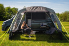 A young woman sits inside the Pershore Breeze® Campervan Canopy by OLPRO the canopy is on a grey Volkswagen T5 & is dressed with camping furniture