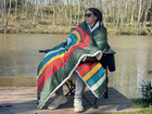 The Original Insulated Blanko® - 2026 Range OLPRO worn as a cape sat on a camping chair by a lake.