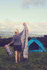 An adult female carrying a Hush Pattern Single Sleeping Bag to a campsite.