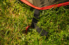 The OLPRO Solo Lightweight Backpacking Tent pegged into the ground using one of the red alloy lightweight pegs.