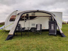 The OLPRO View Lite Breeze 390 Caravan Awning pictured in a Caravan site attached to a caravan with  some camping furniture on display inside of the awning.