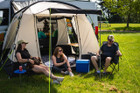A group of people relaxing outside of the Cubo XL Motorhome Awning - Fibreglass Poles that is attached to a Volkswagen Crafter.