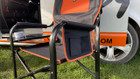 The OLPRO Directors Camping Chair in orange and black with the side table up pictured in front of a VW campervan.