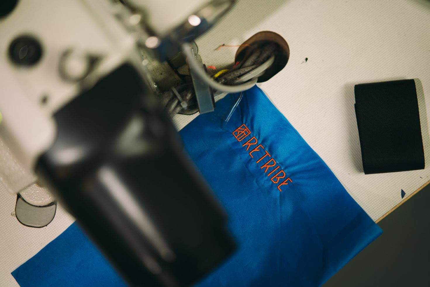 A sewing machine working on blue canvas with the retribe logo in orange