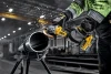 DeWalt DCG410WW1 20V MAX XR brushless angle grinder cutting a steel pipe in an industrial fabrication environment.