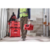 Worker carrying the Milwaukee 48-22-8437 PACKOUT Compact Crate loaded with tools on a construction jobsite.
