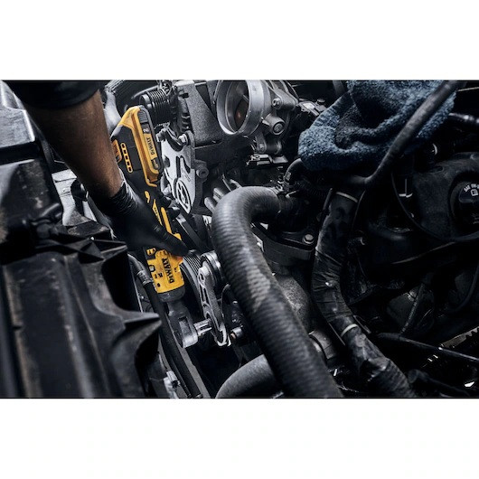 DEWALT DCF513B cordless ratchet being used to remove a bolt inside a crowded automotive engine bay to demonstrate its compact reach.
