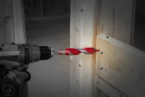 A professional drilling a 7/8-inch hole through a triple-stacked floor joist using a Diablo DAG3090 deep-reach auger bit to show rapid chip evacuation.