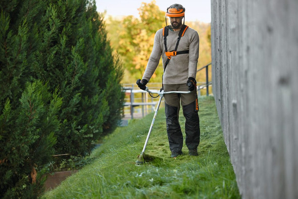STIHL FA082000007 cordless brushcutter with loop handle trimming tall grass on a sloped landscape, providing efficient battery-powered vegetation management.