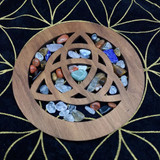 Wooden knotwork disc in basswood with interwoven cutout design, styled on dark cloth with small tumbled stones