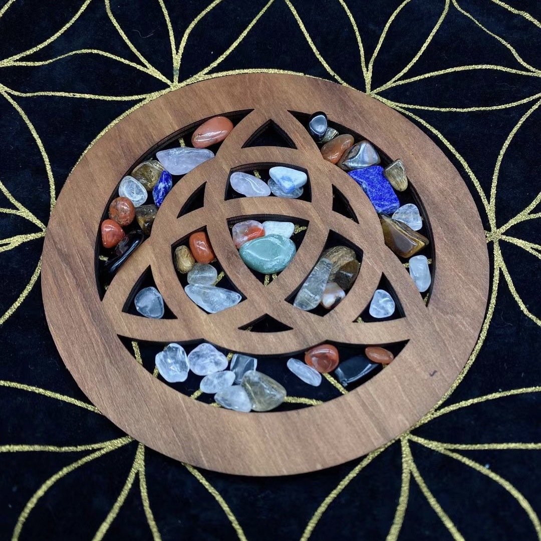 Wooden knotwork disc in basswood with interwoven cutout design, styled on dark cloth with small tumbled stones