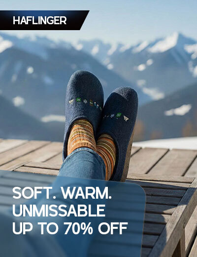Graphic, person relaxing outdoors with feet up in blue HAFLINGER slippers and striped socks against snowy mountain view, text, HAFLINGER Slippers & Boiled Wool Clogs: SOFT. WARM. UNMISSABLE UP TO 70% OFF