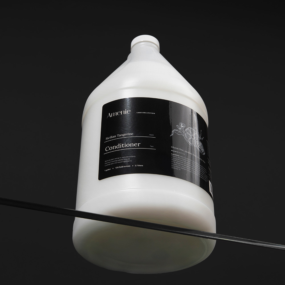 Close-up of Amenie Sicilian Tangerine Conditioner gallon bottle with sleek black background