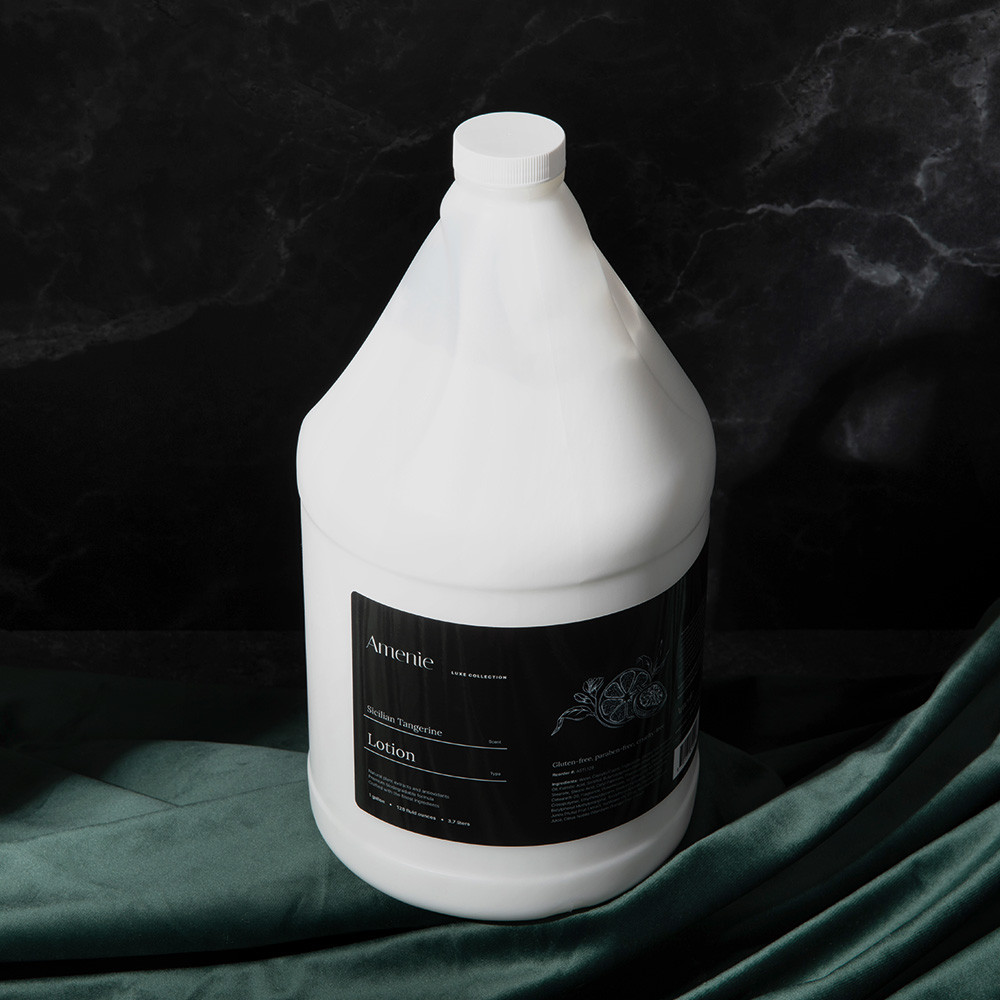 Amenie Sicilian Tangerine Lotion gallon bottle on dark green satin fabric for a spa-inspired setting
